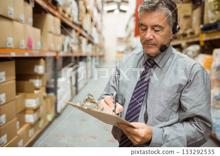 Senior male supervisor in suit with clipboard checking boxes on warehouse racks, copy space Senior male supervisor in suit with clipboard checking boxes on warehouse racks, copy space 133292535