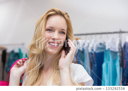Female shopper holding smartphone and pink shopping bag, browsing metal rack in store, copy space 133292556