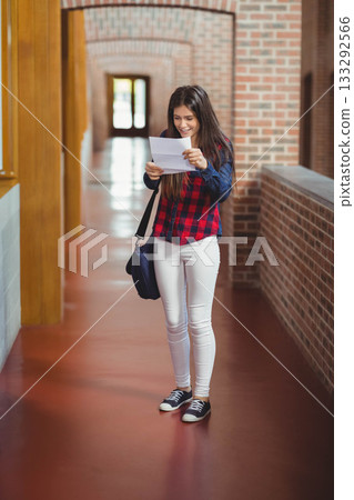 White female student smiling and reading paper in brick hallway with columns, arches, navy bag White female student smiling and reading paper in brick hallway with columns, arches, navy bag 133292566