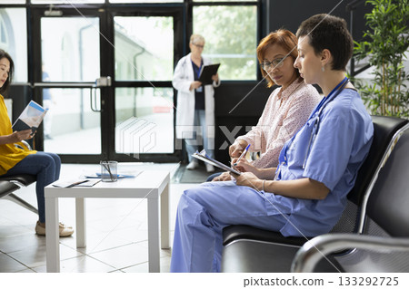 Asian patient chatting with healthcare provider during routine checkup in a lobby, medical guidance and treatment recommendation. Nurse reviews medical history and recovery steps. 133292725