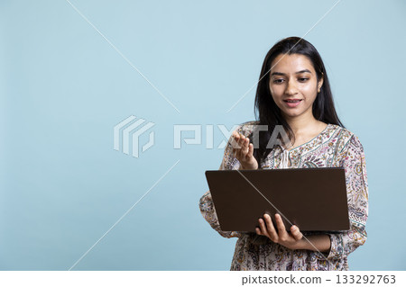 Joyful person gossiping with friends on a video conference call, posing against studio background. Happy relaxed woman bonding with her girls, attend online video call on laptop. 133292763