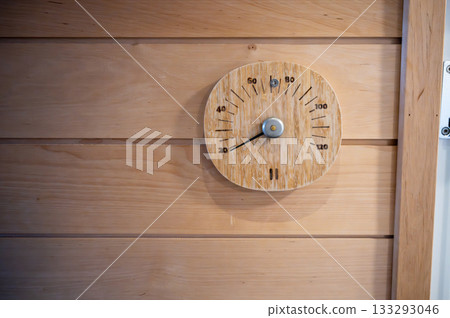Wooden sauna thermometer mounted on light timber wall inside traditional Finnish sauna 133293046