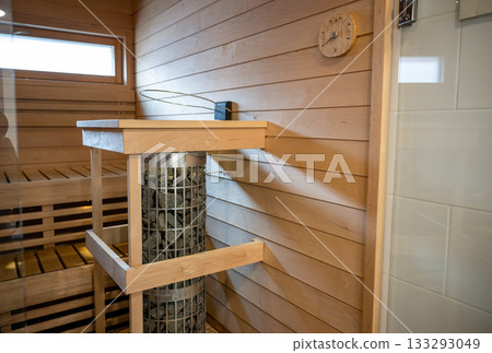 Modern wooden Finnish sauna interior with electric heater, stones and warm cozy ambiance Modern wooden Finnish sauna interior with electric heater, stones and warm cozy ambiance 133293049