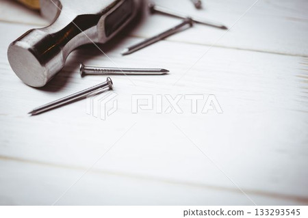 Claw hammer head is resting on white painted wooden surface in 3D render with scattered nails 133293545