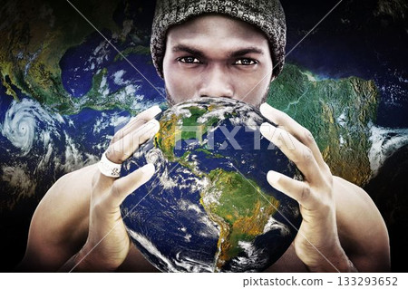 Man wearing beanie and silver ring is holding globe near face against flat backdrop with clouds 133293652