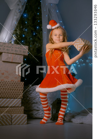 Festive holiday scene with a smiling girl in a Santa outfit presenting a wrapped gift near a Christmas tree Festive holiday scene with a smiling girl in a Santa outfit presenting a wrapped gift near a Christmas tree 133293846