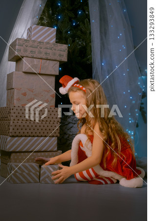 Young woman in a red Santa dress sitting next to a towering pile of beautifully wrapped Christmas gifts indoors. Young woman in a red Santa dress sitting next to a towering pile of beautifully wrapped Christmas gifts indoors. 133293849