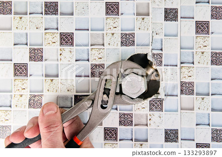 Worker removes steel plug from water inlet pipe preparing connection point for washing machine supply installation in bright utility room. Worker removes steel plug from water inlet pipe preparing connection point for washing machine supply installation in bright utility room. 133293897