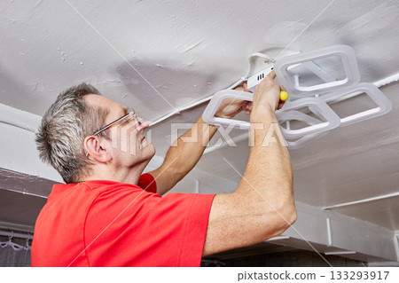 Electrical mounting task involves technician connecting LED chandelier to ceiling in country home as part of lighting installation process. 133293917
