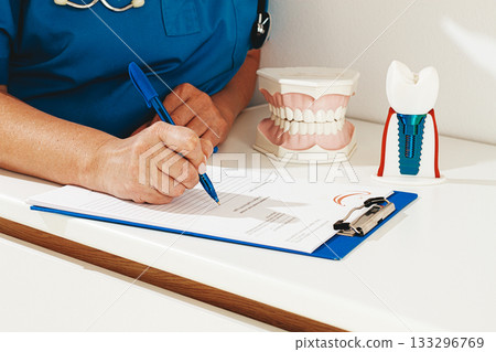 A dentist in a blue uniform studies patient information and prepares for treatment in a modern dental office A dentist in a blue uniform studies patient information and prepares for treatment in a modern dental office 133296769