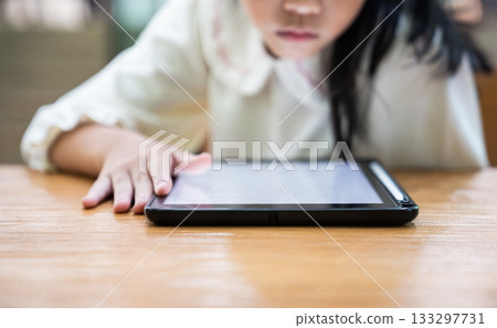 A young child leans closer to the tablet while gently tapping the screen with full attention with a calm moment of exploration and early learning. A young child leans closer to the tablet while gently tapping the screen with full attention with a calm moment of exploration and early learning. 133297731