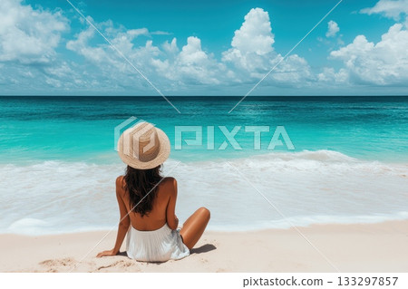 A woman is sitting on the beach wearing a straw hat 133297857