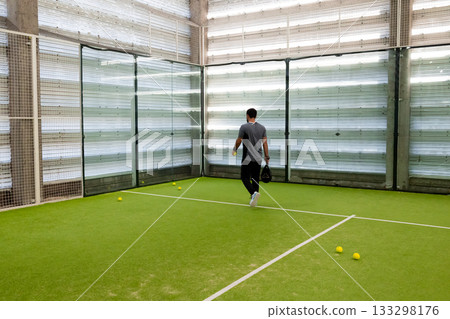 Male practicing tennis on indoor court with equipment 133298176