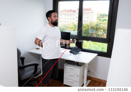 Young caucasian male exercising with resistance band in home office setting 133298186