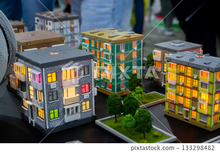 Prototype building printed on 3D printer from melted plastic. 3D-printed building prototype. A house created on 3D printer with green walls, gray roof, and illuminated windows and balconies. 133298482