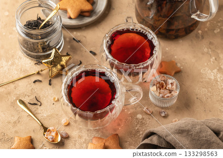 Black tea in two transparent glass cups on brown textured table background with teapot, cookies and ingredients. Cozy breakfast teatime 133298563