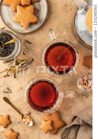 Black tea in two transparent glass cups on brown textured table background with teapot, cookies and ingredients. Cozy breakfast teatime, top view 133298565