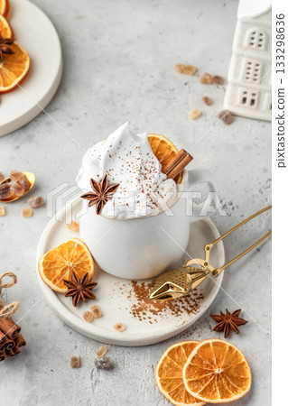 Hot cocoa drink with whipped cream, dried orange and spices in mug on white festive christmas table background 133298636