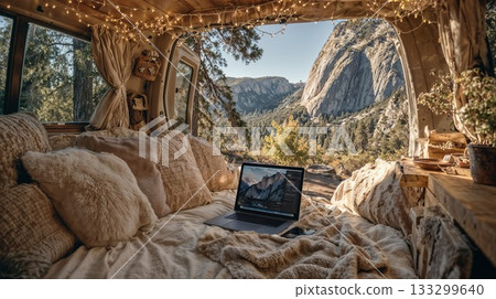 Cozy van life interior with laptop on bed overlooking mountain valley landscape. Comfortable nomadic living space with fairy lights and scenic nature view 133299640
