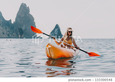 Kayaking Woman Sea - A woman in a yellow bikini paddles a kayak in the ocean with a rocky mountain range in the distance. Kayaking Woman Sea - A woman in a yellow bikini paddles a kayak in the ocean with a rocky mountain range in the distance. 133300548