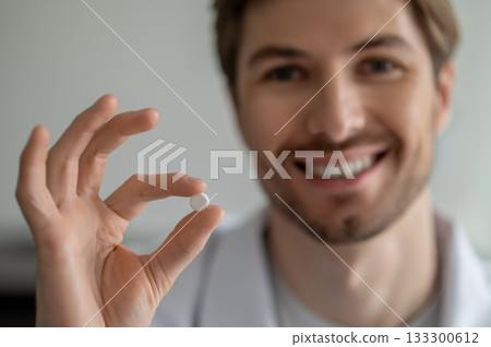 Close-up of smiling man's hand holding small white pill 133300612