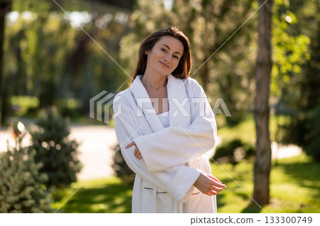 Caucasian dark-haired cute young woman in white robe feeling tranquil and happy Caucasian dark-haired cute young woman in white robe feeling tranquil and happy 133300749