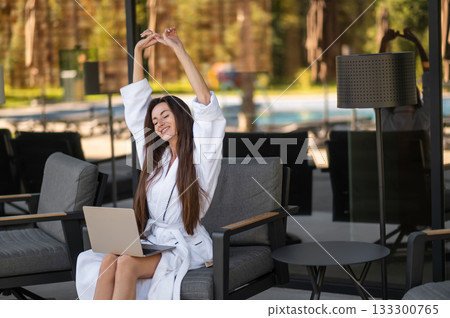Pretty young woman in white bath robe sitting with laptop 133300765