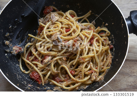 spaghetti with anchovies and cherry tomatoes in black pan on table spaghetti with anchovies and cherry tomatoes in black pan on table 133301519