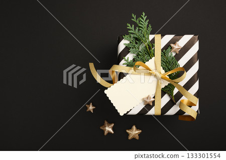 Christmas black and white gift box with empty rectangular tag on black background. Copy space Christmas black and white gift box with empty rectangular tag on black background. Copy space 133301554