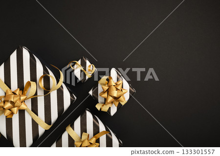White and black striped gifts with golden ribbons on black background. Space for text, congratulations, wishes. 133301557