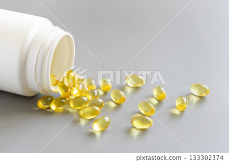 Yellow softgels (gelatin capsules) and bottle on a grey close up. Omega 3 Fish oil or garlic oil Yellow softgels (gelatin capsules) and bottle on a grey close up. Omega 3 Fish oil or garlic oil 133302374