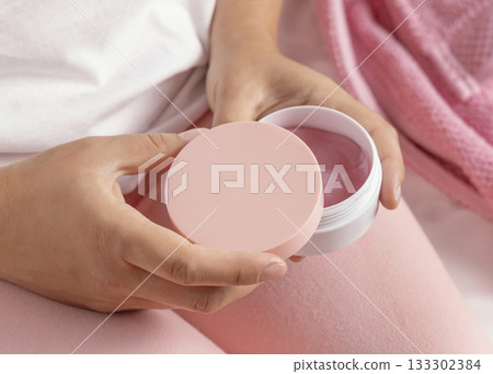 Closeup of woman in pink pyjamas holding cosmetic jar with blank lid in hands, mockup Closeup of woman in pink pyjamas holding cosmetic jar with blank lid in hands, mockup 133302384