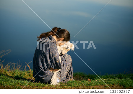 Woman kiss and hug her cute white dog sitting on grass over scenic mountain background 133302857