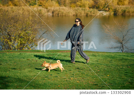 Smiling woman having fun walking and playing with her dog near lake Smiling woman having fun walking and playing with her dog near lake 133302908