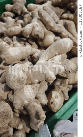 Fresh ginger roots with rough beige skin displayed in a crate at a farmers market. Concept of medicinal food, natural remedies and culinary spice Fresh ginger roots with rough beige skin displayed in a crate at a farmers market. Concept of medicinal food, natural remedies and culinary spice 133303167