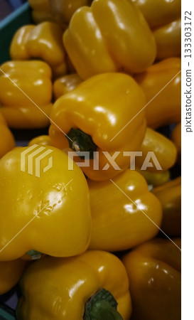 Bright yellow bell peppers with glossy skins stacked in a green crate at a fresh produce market. Concept of healthy eating, vitamin-packed vegetables and colorful seasonal food Bright yellow bell peppers with glossy skins stacked in a green crate at a fresh produce market. Concept of healthy eating, vitamin-packed vegetables and colorful seasonal food 133303172