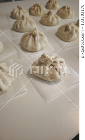 Uncooked homemade bao buns resting on parchment squares before steaming. Concept of traditional food preparation, Asian cuisine and handmade dumplings 133303176