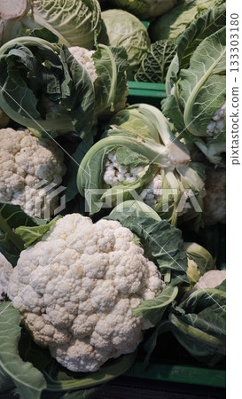 Fresh heads of white cauliflower with green leaves displayed in a market crate under natural light. Concept of organic farming, vegetarian food and seasonal local harvest Fresh heads of white cauliflower with green leaves displayed in a market crate under natural light. Concept of organic farming, vegetarian food and seasonal local harvest 133303180