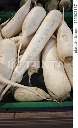 Fresh white daikon radishes stacked in a green crate at a farmers market under natural light. Concept of detox food, healthy eating and seasonal root vegetables 133303187