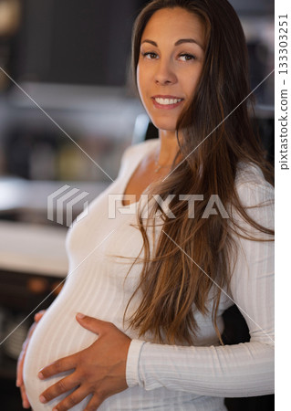 Smiling pregnant woman poses in cozy home setting emphasizing maternity charm 133303251
