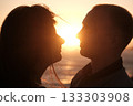 Silhouetted couple facing each other with the setting sun between them, creating a romantic and intimate golden hour moment. 133303908