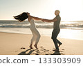 Young couple playfully spinning on the beach at sunset, laughing and enjoying a carefree romantic moment by the ocean. 133303909