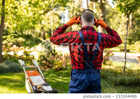 Man standing in park holding headphones while working as gardener Man standing in park holding headphones while working as gardener 133304490