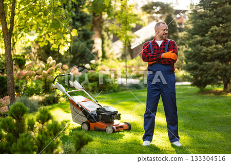 Gardener posing with lawnmower in backyard area 133304516