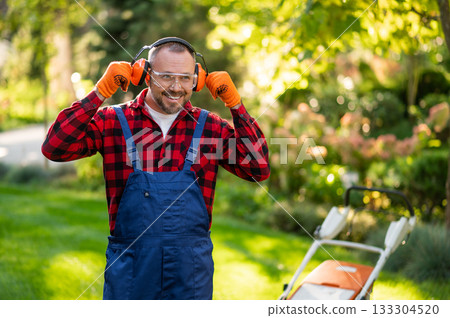 Male gardener adjusting protective earmuffs during lawn maintenance Male gardener adjusting protective earmuffs during lawn maintenance 133304520