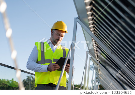 Man at renewable energy station controlling equipment through digital device 133304635