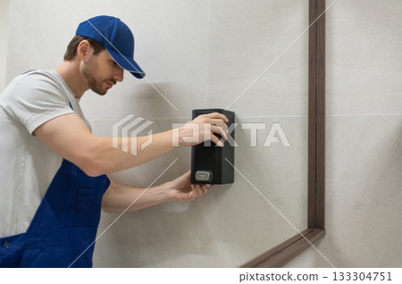 Worker fixing wall mounted soap dispenser in modern bathroom 133304751