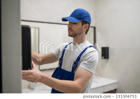 Maintenance technician installing new hand dryer on tiled wall 133304753