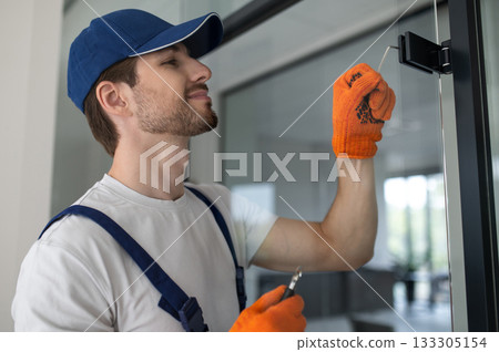 Male installer securing hinges and hardware on glass door Male installer securing hinges and hardware on glass door 133305154