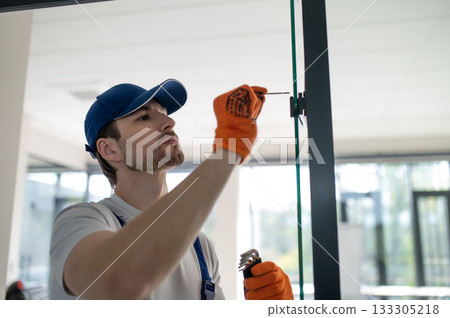 Worker fitting handles and locks on glass partition 133305218